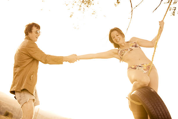 jovem casal brincando em um balanço de corda ao pôr do sol - men swing tire rope swing imagens e fotografias de stock