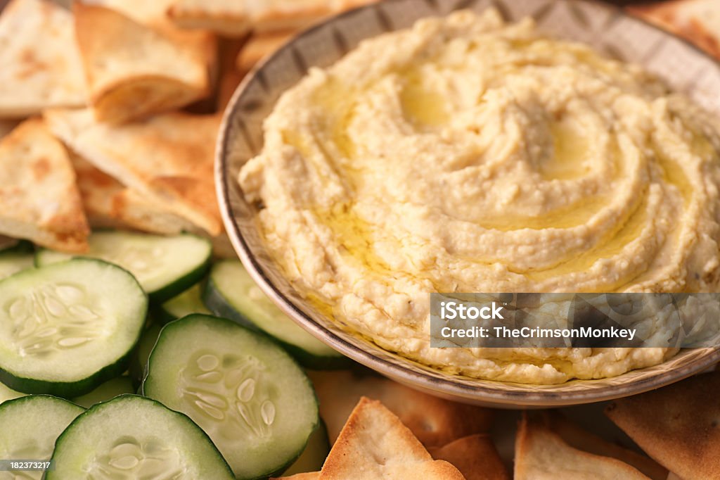A bowl of fresh hummus and cucumbers High-resolution, full-frame, close-up digital capture of a bowl of freshly made hummus with sliced Arabian cucumbers and golden toasted pita points. Surface of hummus is drizzled with extra virgin olive oil. Hummus - Food Stock Photo