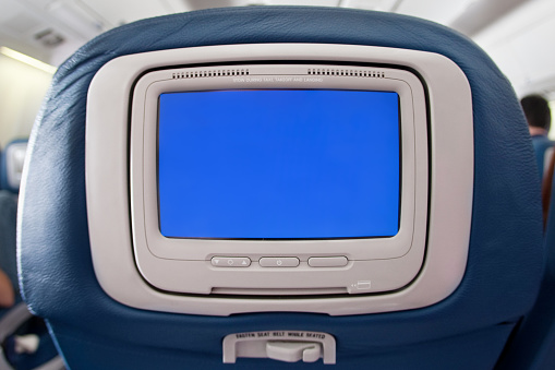 Modern airplane seat with individual  monitor with blank blue display.