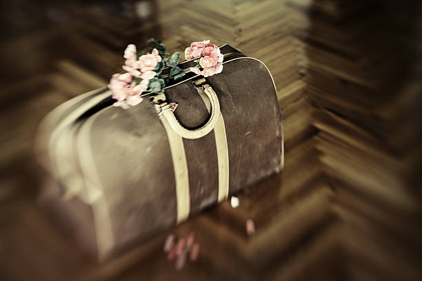 Pink geraniums are sticking out of an old doctor's bag. Some petals on the parquet floor. Image is shot with Lensbaby. Colors are manipulated and desaturated.