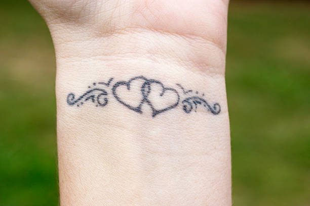 Linked hearts tattoo on wrist Wearer's own design for a linked hearts tattoo which decorates her left wrist. Close up taken in natural daylight. wrist tattoo stock pictures, royalty-free photos & images
