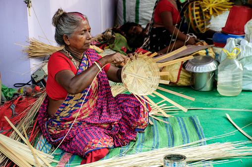 Kolkata, west Bengal. An old woman making basket by bamboo fiber for house hold use. Selling in a handicraft fair in the city.
