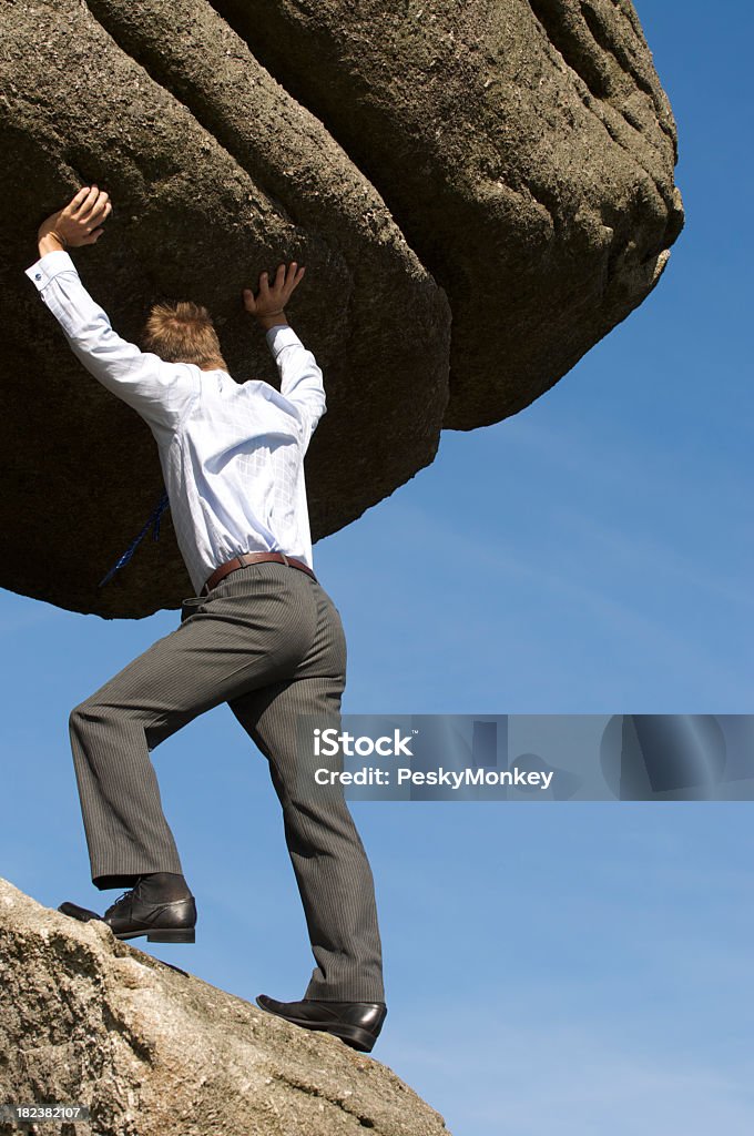 Прочные бизнесмен, сражавшиеся толкать Boulder Up - Стоковые фото Stuck between a rock and a hard place - английское выражение роялти-фри