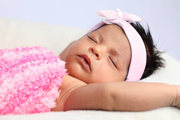 Newborn baby girl wrapped in pink blanket wearing pink bow.