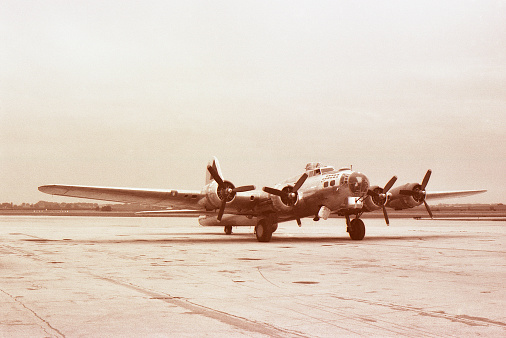 WWII bomber on taxiway. B-17. Black and white film naturally faded to sepia. Scanned film with significant grain.