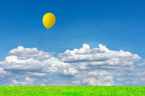 Yellow balloon floating in the blue sky over the green hill with copy space.