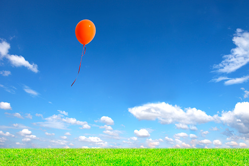 Orange balloon floating in the blue sky over the green hill with copy space.