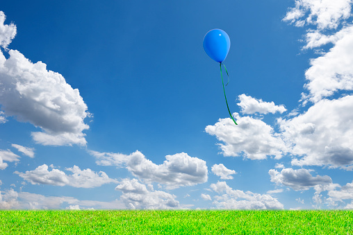 Blue balloon floating in the blue sky over the green hill with copy space.