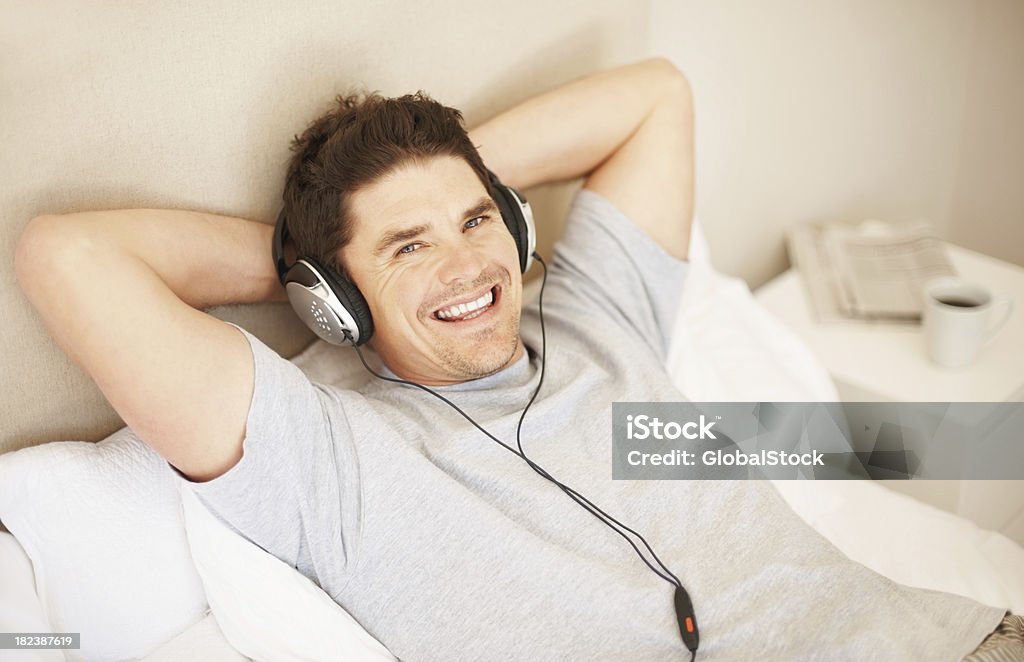 Felice bell'uomo ascoltando la musica a letto - Foto stock royalty-free di 35-39 anni