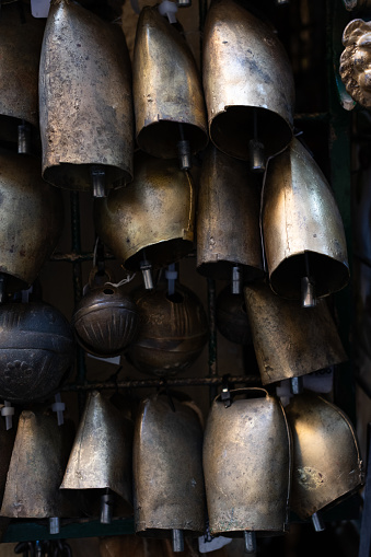 Numerous golden, dirty, metal bells or chimes hanging on a hook outside a shop in Tuscany, Italy.