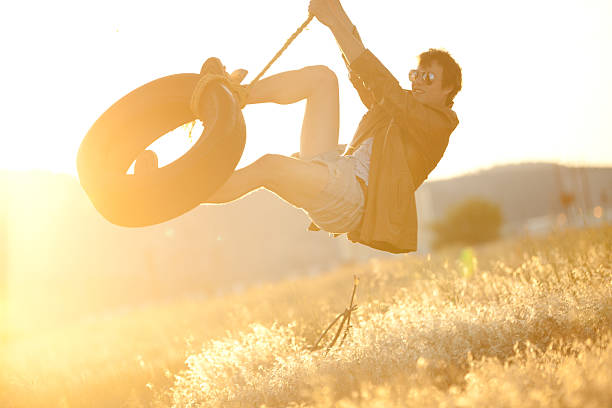 junge hipster schwingen auf seilschaukel bei sonnenuntergang - men swing rope swing tire stock-fotos und bilder