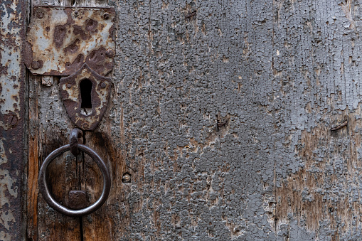 Detail of an aged, worn and weathered wooden doorway with keyhole, knocker ring, cracked wood and a rough texture.