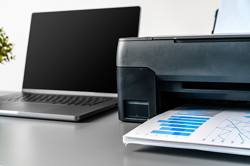 Printer and laptop on grey table in office close up