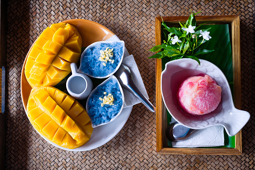 Mango sticky rice is purple in color from the natural color of the butterfly pea flower, beautifully placed on a woven bamboo tray. Sweet pickled caranda in ice Placed on a woven bamboo tray.