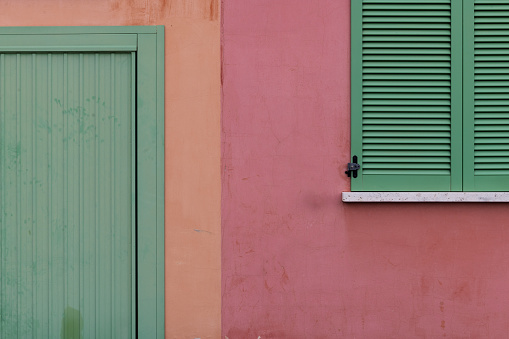 An exterior section of an Italian apartment building artfully painted in green, orange and pink paint.