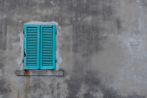 Brightly colored, turquoise, wooden shutters closed in on a large, gray cement wall on a building in Tuscany, Italy.