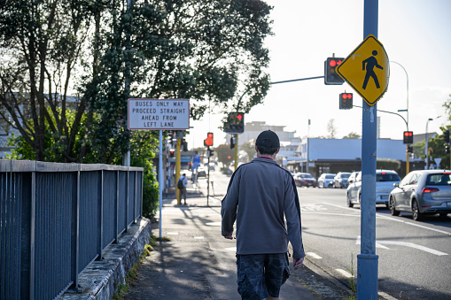 Man walking on the pedestrian sidewalk of the city street. Road signs and traffic lights at the intersection. Auckland.