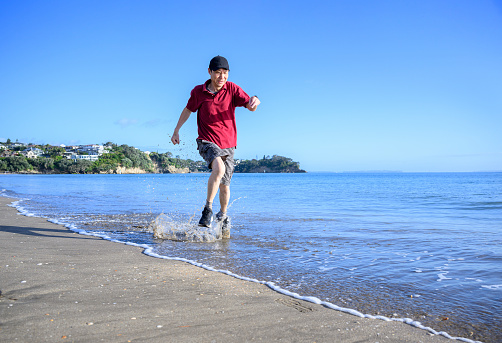 Man running in water on Milford Beach. Auckland.