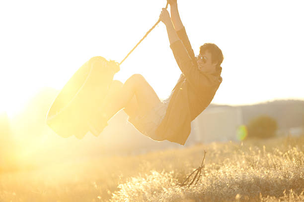 junge hipster schwingen auf seilschaukel bei sonnenuntergang - men swing rope swing tire stock-fotos und bilder