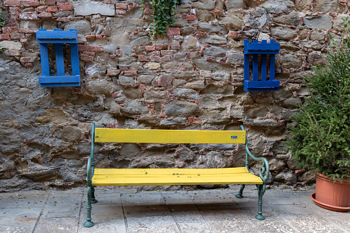 A yellow wooden bench set between two wood palettes painted blue and mounted to an aging stone and brick wall in Sinalunga, Tuscany, Italy.