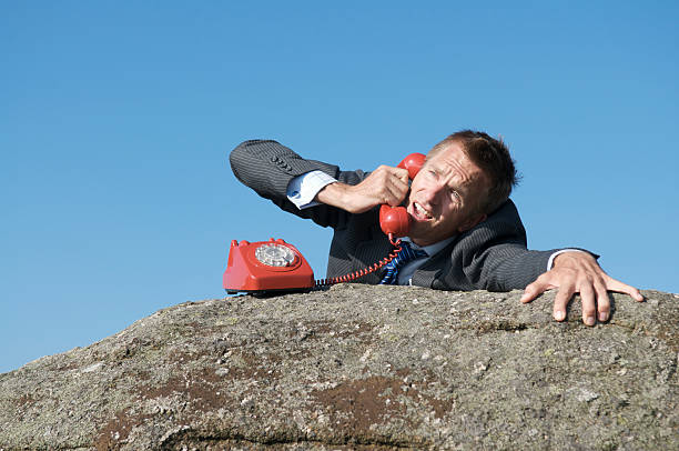 desesperado hombre de negocios en la cima de la llamada telefónica del rock - dropped call fotografías e imágenes de stock