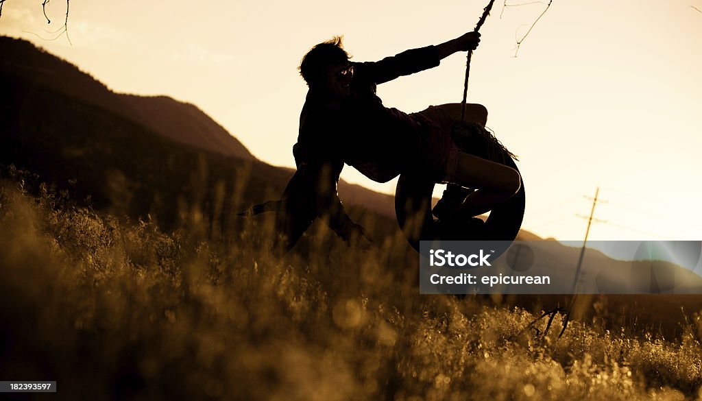 Jeune homme sur la corde swing au coucher du soleil - Photo de Balançoire pneu libre de droits