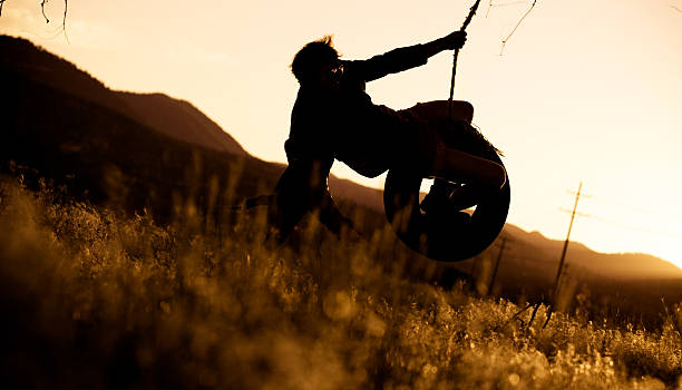 jovem de baloiço de corda ao pôr do sol - men swing tire rope swing imagens e fotografias de stock