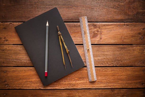 Closed old notebook, pencil, ruler and drawing compas on a rustic wooden board