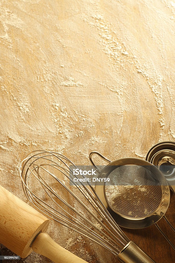 Baking Utensils "A basket of eggs,an egg whisk,a flour sifter,measuring spoons,and a chef's hat on a cutting board covered with a dusting of flour." Baking Stock Photo