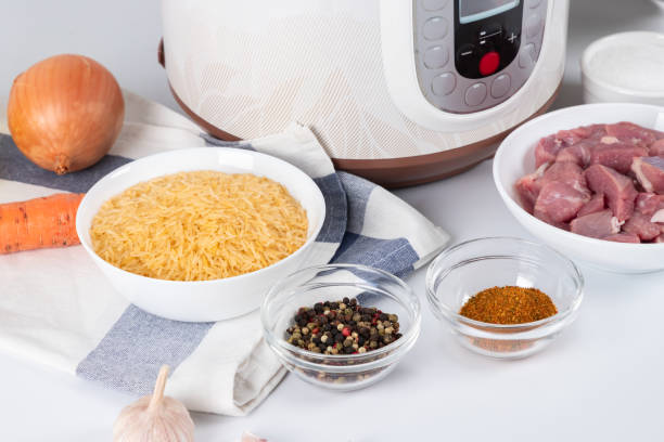 istock Prepared ingredients for cooking pilaf in modern multi cooker in kitchen on a table. Cooking pilau with meat in multicooker. 1823989904