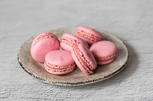 Traditional French macaroons. Pink almond cookies on a stylish ceramic plate on a gray stone background. Delicious dessert.