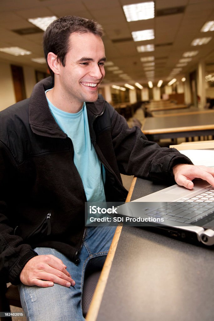 Sorridente studente di College utilizzando il computer portatile in biblioteca della scuola - Foto stock royalty-free di 20-24 anni