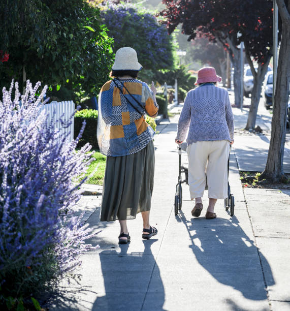 istock Senior woman walking using a mobility walker on the pedestrian footpath, accompanied by her daughter. Vertical format. 1824024296