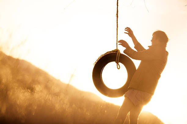 jovem hipster balançar de baloiço de corda ao pôr do sol - men swing tire rope swing imagens e fotografias de stock