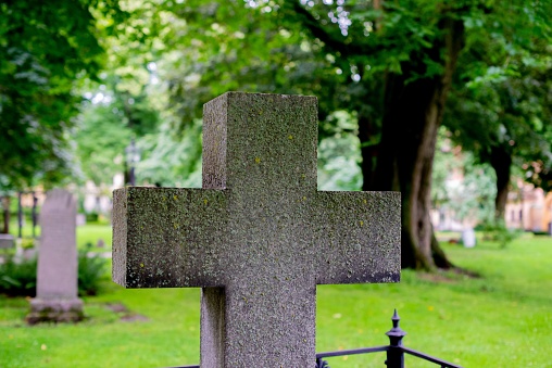 A cross in the center of a grassy cemetery, surrounded by trees