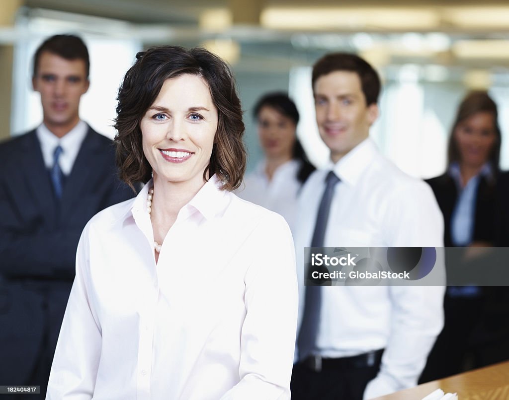 Sorridente Adulto di mezza età donna d'affari con i colleghi in background - Foto stock royalty-free di 20-24 anni