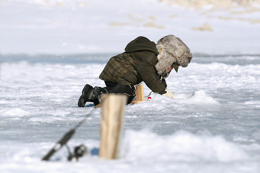 Little boy looking down a hole while ice fishing