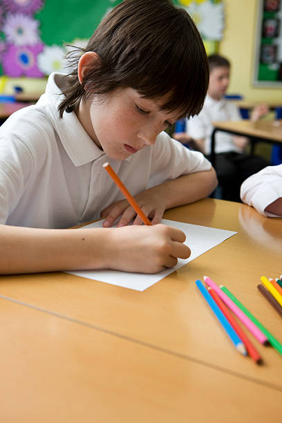 istock A boy using colored pencils at his desk to draw at school. 182407808