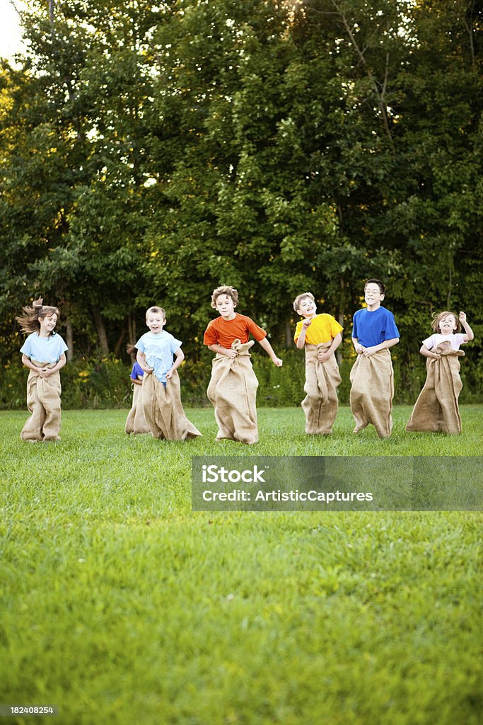 Happy Children Having a Fun Potato Sack Race Outside Color photo of a group of happy kids laughing and enjoying a potato sack race outside. Jumping Stock Photo