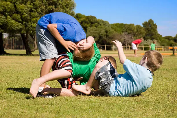 Three little boys play fighting in the park.