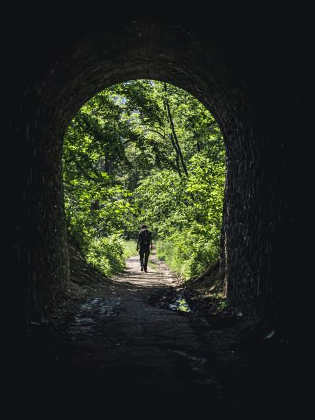 One single man walking out of a tunnel into a forest, hiking equipment, backpack