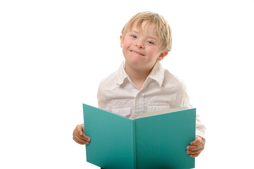 Seven year old boy with Down Syndrome dressed in a white blouse reads a turquoise book. White background.More photo's of this boy: