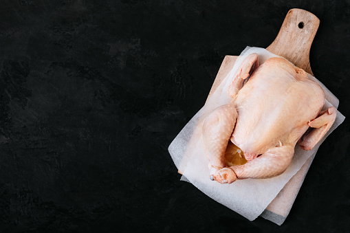 Whole Raw Chicken ready to cook. Dark black background, copy space, top view