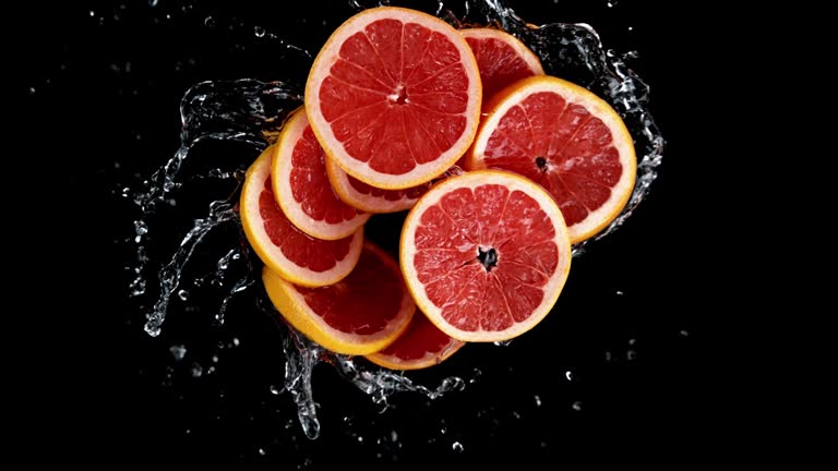 Super Slow Motion of Rotating Grapefruit Slices Into Water on Black Background.