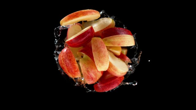 Super Slow Motion of Rotating Red Apple Slices Into Water on Black Background.