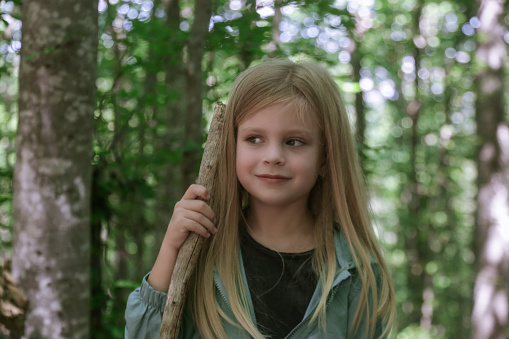 Candid portrait of a smiling young woman sitting in a field with forest in the background