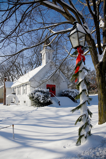 A small white country church located in rural Maryland.  Photo was taken just after a heavy snowfall.  Streetlights in the town are decorated for the holiday.  Deep snow covers the ground.