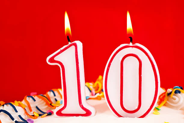 istock Decorated birthday cake with number 10 burning candles.  Red background 182413832