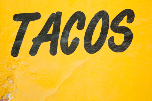 Black hand-painted sign on yellow grunge wall advertises tacos.