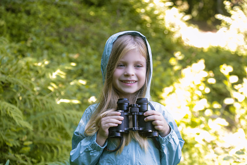 Cute little girl exploring nature looking through binoculars. Child playing outdoors. Kids travel, adventure and bird watching concept.